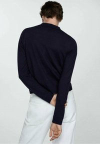 Námorně modrý pletený svetr s dlouhými rukávy, oblé límcem a žebrovanými manžetami. Nosený s bílými kalhotami, ukazuje jednoduchý a čistý design.