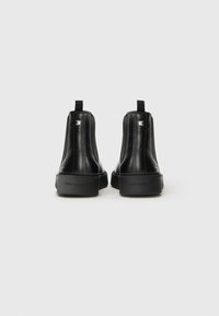 Botas de tobillo de cuero negro con un diseño elegante, punta redondeada, acabado texturizado y un sutil acento del logo en el tacón.