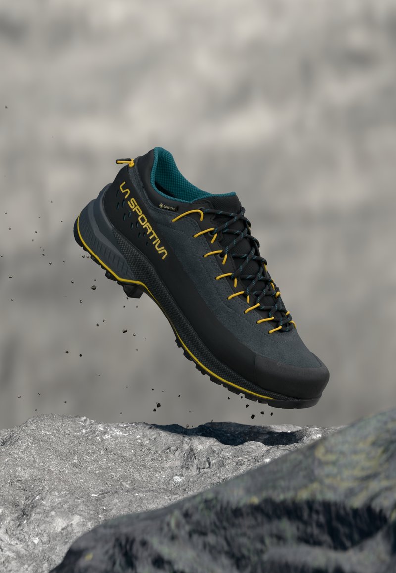 Μαύρο υπαίθριο παπούτσι με γκρι επάνω μέρος από σουέντ, κίτρινα κορδόνια και τυρκουάζ γιακά. Διαθέτει ανάγλυφη σόλα και οπές αποστράγγισης. Ελαφρύ και ανθεκτικό σχεδιασμό.