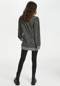 Felpa grigia con stampa leopardata, maniche lunghe, polsini e orlo a coste; abbinata a jeans skinny neri e stivali neri alla caviglia.