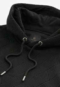Hoodie noir texturé avec cordons de serrage ornés d'embouts métalliques et étiquette de marque "NEXT" à l'intérieur du col.