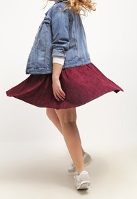 Jeansjacka med en figursydd kropp och långa ärmar, kombinerad med en vinröd knä-lång kjol av texturerad tyg och vita sneakers.