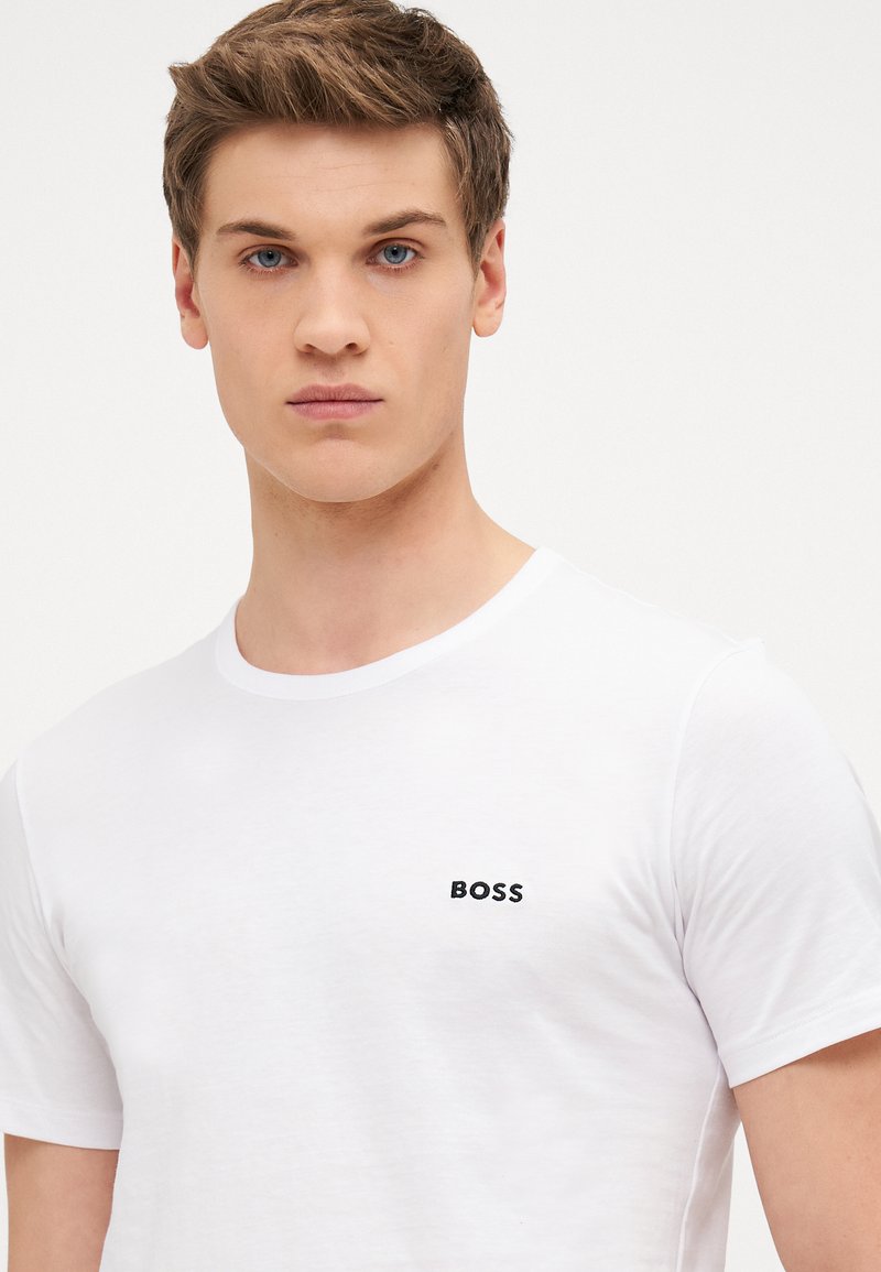 T-shirt blanc à col rond en coton, avec un petit logo noir "BOSS" sur la poitrine, à manches courtes et à coupe standard.