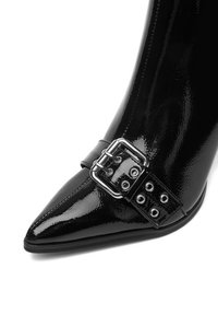 Czarne lakierowane botki z długim noskiem, z szerokim srebrnym paskiem z klamrą z przodu oraz przeszyciami.