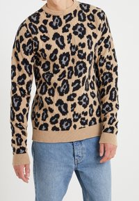 Beige stickad tröja med leopardmönster i svart och grått, med ribbat nacke, ärmar och nederkant. Mjuk textur, figurnära design.