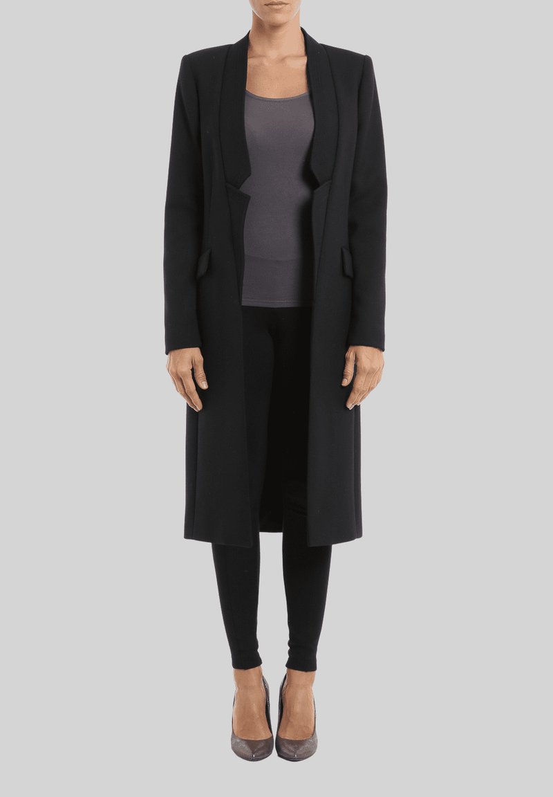 Abrigo largo negro con un diseño a medida, que cuenta con un cuello de chal, dos bolsillos frontales y forrado con un interior suave, llevado sobre una camiseta oscura y leggings.