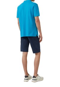 Helles blaues Poloshirt und marineblaue Shorts mit Kragen, kurzen Ärmeln und seitlichen Schlitzen für mehr Bequemlichkeit. Getragen mit hellen Turnschuhen.