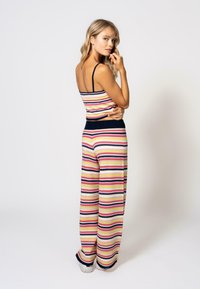 Stripet strikket to-delt antrekk med en tettsittende tanktopp og brede bukser. Fargene inkluderer marineblå, rosa og krem. Teksturt stoff med tynne stropper.
