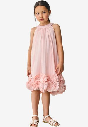 Abito halter rosa chiaro con tessuto fluido, scollatura arriccita e decorazioni floreali all'orlo. Il modello indossa sandali flat.