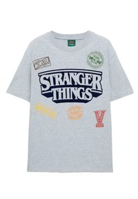 Szara koszulka z krótkim rękawem z napisem "STRANGER THINGS" w granatowym kolorze, z różnymi kolorowymi nadrukowanymi odznakami i logo na przodzie.
