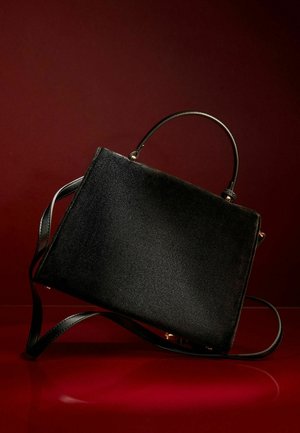 Black handbag made of textured material, featuring two handles, a removable strap, and gold hardware accents. Rectangular shape.