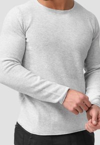 Gray long-sleeve shirt with a textured knit fabric. Features a round neckline and fitted sleeves, with a slightly curved hemline.