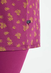 Top morado con estampado de flores amarillas y rayas horizontales, acompañado de leggings morados sólidos. Etiqueta de marca visible en la costura.