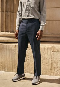 Navy pinstriped trousers made of fabric with a smooth texture, paired with gray athletic shoes and a light gray button-up shirt.
