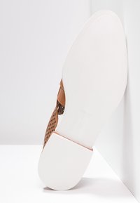 Sandalo in pelle perforata marrone con fascia ampia, suola in gomma bianca e forma arrotondata, che mostra dettagliata texture e caratteristiche di design.