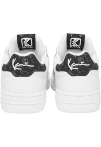 Fehér sportcipők, textúrált fekete sarka emblémával, párnázott gallérral és kontrasztos fehér talppal.