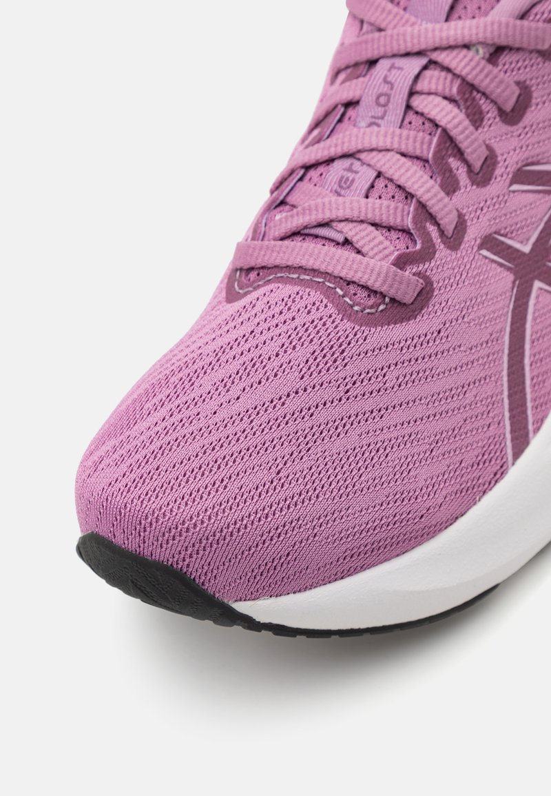 Zapatilla atlética ligera de malla morada con superficie texturizada, que presenta cordones planos y una suela de goma con acentos negros.