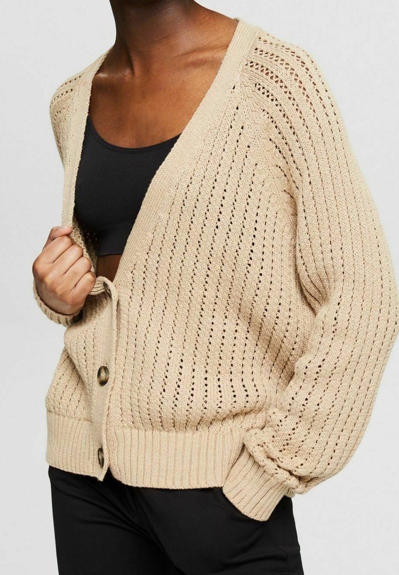 Beige gestrickte Strickjacke mit lockerem Sitz, V-Ausschnitt, vertikalen Streifen und Knöpfen auf der Vorderseite. Strukturierte offene Webart verleiht optisches Interesse.