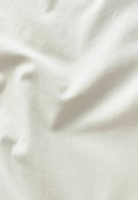 Tissu beige clair avec une surface douce et texturée, montrant des rides et des plis naturels. Le matériau semble lisse et uni.