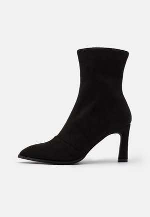 Bottine en suede noire avec un bout pointu, un talon haut et une texture lisse. Présente un design ajusté s'étendant au-dessus de la cheville.