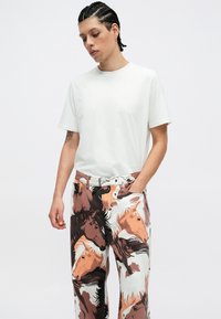 Fehér, kerek nyakú póló, amely laza szabású nadrággal van párosítva, amelyen barna, narancssárga és fehér árnyalatú ló mintázat látható; a textúra sima.