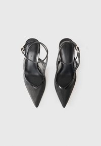 Chaussures noires à bout pointu et à talon ouvert, présentant une finition en vernis brillant, des panneaux en mesh et une fine bride de cheville avec une boucle en métal.