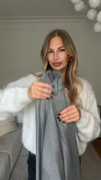 Graues Stoffkleidungsstück, das in den Händen gehalten wird, mit einer weichen Textur und einem lockeren, drapierten Design. Heller Hintergrund und gemütliche Atmosphäre verbessern die Sichtbarkeit.