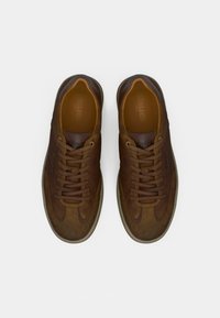Las zapatillas deportivas de cuero marrón presentan una puntera redondeada, una parte superior texturizada y cordones en tonos con un sutil logotipo cerca de la entresuela. Diseño de perfil bajo.
