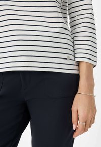 Gestreiftes langärmliges Oberteil in Weiß und Marineblau, kombiniert mit dunkelblauen Hosen. Mit einem silbernen Akzent am Saum und einer glatten Stofftextur.