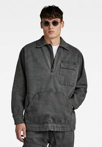 Sivkasta denim pulover s polovičnim zadrgo na sprednji strani, ovratnikom, ki se prepogne, in žepom na prsih, z kenguru stilom sprednjega žepa ter sproščenim prileganjem.