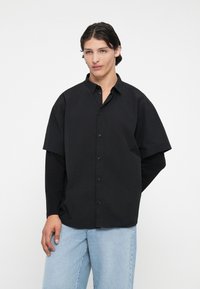 Camiseta preta de manga curta com botão frontal e corte descontraído, combinada com jeans de denimo azul claro. Tecido suave e textura sutil.