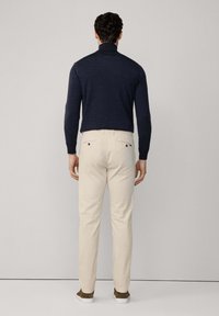 Granatowy sweter z golfem w połączeniu z kremowymi chinosami. Spodnie mają dwie tylne kieszenie z ciemnymi guzikami, a całość uzupełniają brązowe buty.