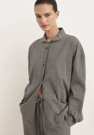 Chemise oversize à carreaux noir et blanc avec col, boutons à l'avant et poches latérales. Le tissu a l'air texturé et doux.