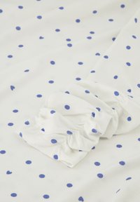 Witte stof met blauwe stippen, met een details van geplooide mouwen. Zachte, lichte textuur, gelijkmatig verdeelde stippen.