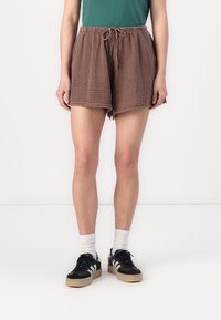 Brown, textured shorts with an elastic waistband and drawstring. Paired with black sneakers and white crew socks, standing on a plain background.