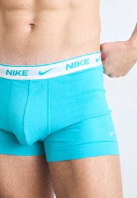 Nike men's boxers in bright turquoise, made of soft cotton blend, featuring a white elastic waistband with blue Nike branding and logo.