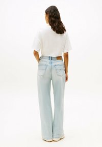 Top blanco de manga corta combinado con jeans de pierna ancha azul claro, con un parche de cuero en la cintura y dos bolsillos traseros.