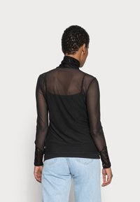 Top nero a maniche lunghe con tessuto trasparente e testurizzato sulle maniche e sulla schiena, con scollatura alta e forma aderente. Abbinato a jeans azzurri.