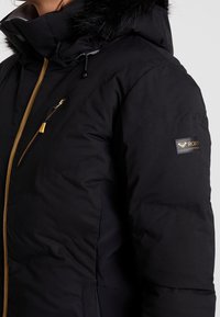 Svart pufferjacka med huva i fuskpäls, gyllene dragkedjor och Roxy-logotyp på ärmen. Strukturerad textil med vanlig passform.
