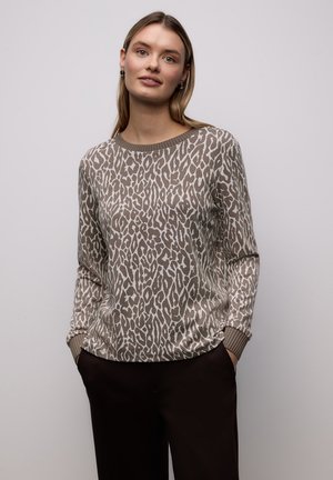 Pull beige avec un imprimé léopard en marron et crème. Encolure ronde et poignets côtelés. Associé à un pantalon marron foncé.