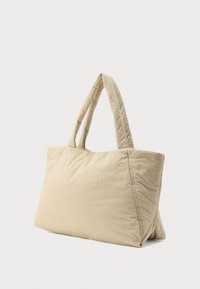 Μπεζ τσάντα ώμου με καπιτονέ ύφασμα, φαρδιές επενδυμένες λαβές, ορθογώνιο σχήμα και απαλό, υφή υφάσματος.