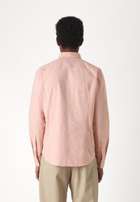 Helles rosafarbenes Langarmhemd aus weichem Stoff, mit klassischem Kragen, Knopfmanschetten und geradem Saum. Die Rückansicht zeigt ein schlichtes Design.