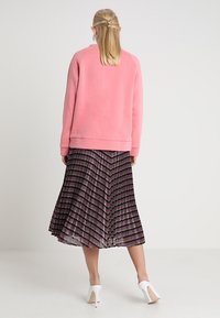 Sudadera rosa con mangas raglán combinada con una falda negra plisada que presenta patrones de rayas coloridas y unos zapatos de tacón blanco.