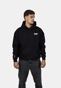 Felpa nera con cappuccio, dotata di tasca a marsupio frontale, con logo bianco sul petto e una piccola grafica bianca sul polsino. Materiale in cotone.