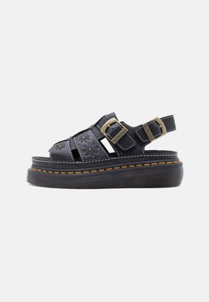 Schwarze Plateausandale aus Leder mit floralen Ausschnitten, doppelten Messingschnallen und gelber Naht auf dicker Gummisohle.