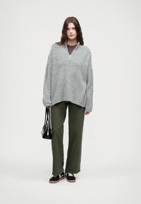 Γκρι υπερμεγέθη πλεκτή μπλούζα με μισό φερμουάρ, ελαιόχρωμες φαρδιές παντελόνες, μαύρη τσάντα χειρός και αθλητικά παπούτσια με λευκές λεπτομέρειες.