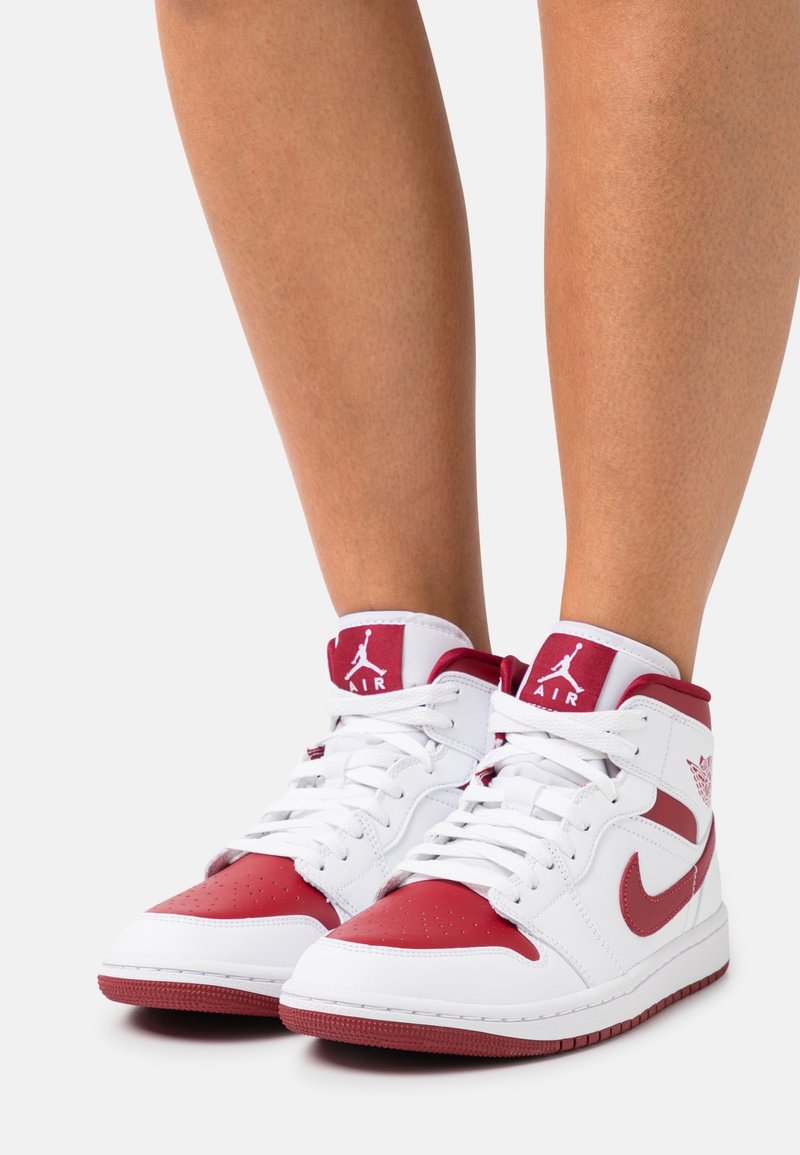 Zapatillas altas blancas y rojas con materiales de cuero y malla, que presentan área delantera perforada, prominente símbolo Nike Swoosh y detalles con el logo Air.