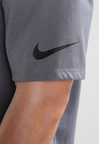 Camisa gris de manga corta con una textura suave y un logo negro de Nike en la manga izquierda. Costuras limpias y diseño casual.