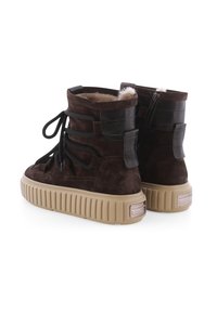 Braune Wildleder-Stiefeletten mit strukturierten Gummisohlen, Schnürung an der Vorderseite und Reißverschlussdetail. Mit fellgefüttertem Innenleben und braunen Lederakzenten.