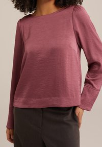 Halenka s dlouhými rukávy z měkké, texturované tkaniny v burgundské barvě. Disponuje výstřihem do "výstřihu" a jemnými sklady na ramenou, stylizována s tmavými kalhotami.